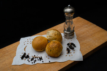 Freshly baked pepper bread presented on a wooden board along with raw pepper and pepper shakers.