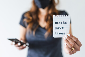 covid-19 pandemic outbreak, woman holding Masks save lives text towards the camera while browsing on her smartphone