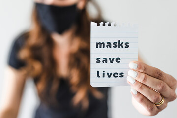 covid-19 pandemic outbreak, woman holding Masks save lives text towards the camera shot at shallow depth of field