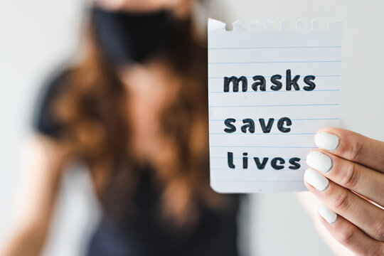 covid-19 pandemic outbreak, woman holding Masks save lives text towards the camera shot at shallow depth of field - Powered by Adobe