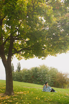 Couple wrapped in blanket sit under tree on autumn day