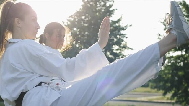 Young women in white kimonos train against the backdrop of nature and hone their karate skills. Side view. Close-up. Slow motion