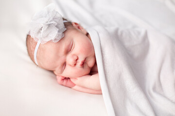 Newborn Baby Girl Sleeping Peacefully Under Blanket, Wearing Flower Headband