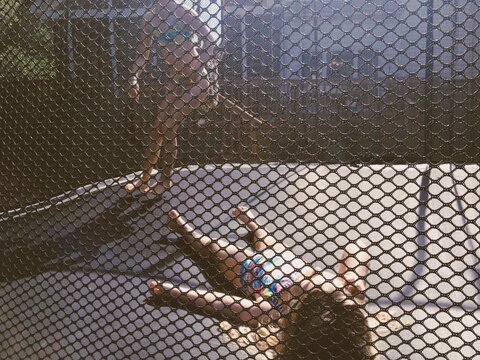 Two girls play on a trampoline.