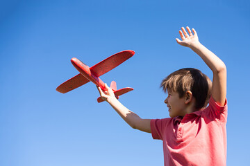 boy playing with a red plane against the sky. Happy childrens games. © Irina