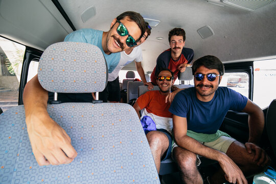 Four young men friends with funky sunglasses in a minivan ready for a road trip during their vacation travel