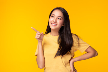 Beautiful young Asian woman pointing up to copy space and looking at copy space with smile face and happy. Pretty girl act like a satisfied product, use for advertising with yellow background