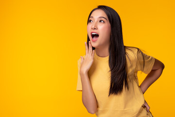 Pretty girl gets surprised when look at copy space. Surprised happy beautiful asian woman looking copy space in exciting. Isolated on yellow background