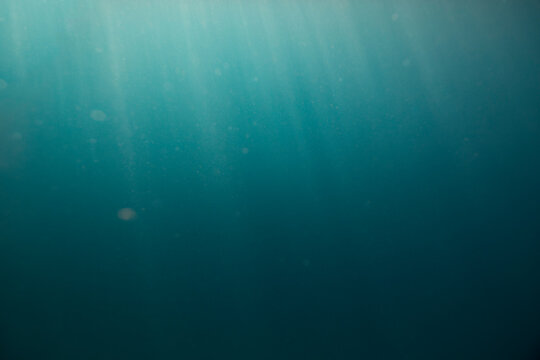 Dark blue under water empty sea background with sunrays going trough the surface