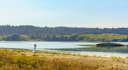 Distant person taking photographs on a misty autumn day on an ocean shore with yellow flowers and grasses - Colwood, Vancouver Island, British Columbia, Canada