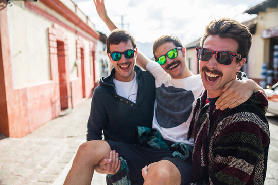 Three young friends wearing sunglasses having fun taking one in their linked arms like a chair in a traditional mexican village