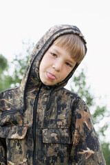 frustrated boy in camouflage uniform shows tongue, upset at losing war game
