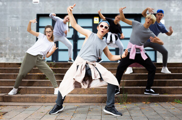 Portrait of modern teenager performing street dance with group of friends outside in summer.