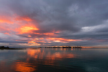 fiery glow of sunset among dense gray cumulus clouds over the green ocean and the silhouette of...