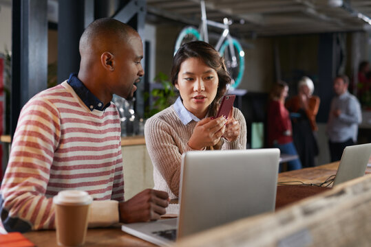Beautiful Asian girl showing African businessman syncronised data on smart moblie device from laptop presentation in cycling showroom