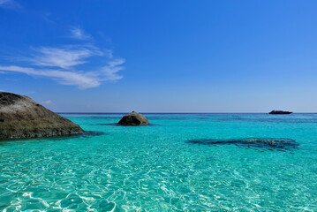 Turquoise Andaman Sea and azure sky with light clouds. Boulders in crystal clear water. There is a boat on the horizon. Summer in Thailand. Similan Islands.