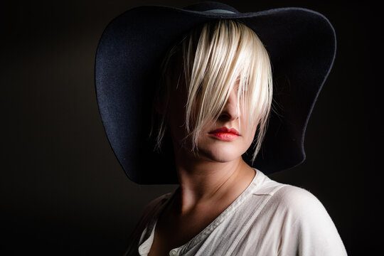 A caucasian woman with short blond hair wearing a hat hiding her face behind her hair.