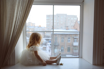 a little girl in a smart, fluffy white dress with a magic wand in her hands near the window and...