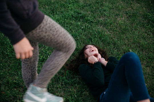 Girl lying on the grass laughing while her sister is standing next to her