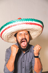 Retrato de hombre joven mexicano hispano latino con sombrero gritando con felicidad emoción dia de...