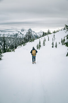 Man Wearing Backpack And Beanie Following Path Through Snowy Mountain Forest