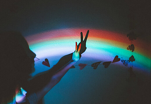 Teenage girl holding her hand up in the shape of a peace sign against a rainbow