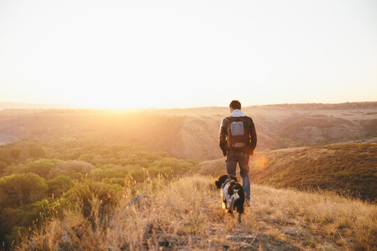 Back view of man and his dog meeting the sunrise