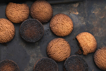 Burnt cookies. Burnt oatmeal cookies lie on a black baking sheet.
