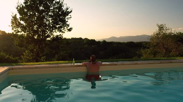 Aerial view of young male adult relaxing swimming pool panoramic scene at sunset in tuscany italy shot in 4k