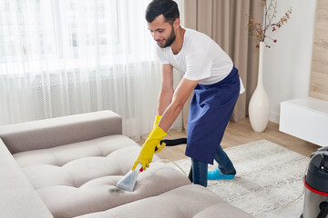 Close-up of housekeeper holding modern washing vacuum cleaner and cleaning dirty sofa with...