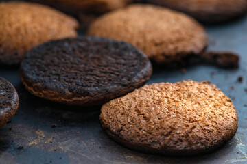 Burnt cookies. Burnt, burnt oatmeal cookies lie on a black baking sheet. Vertical photo