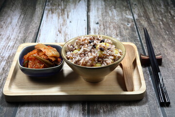 Traditional breakfast set, cooked jasmine rice with bean, gingko, mixed grains and shrimp serving with pickled vegetable (kimchi) on the wooden plate. Selective focus concept. 