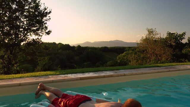 Aerial view of young male adult relaxing swimming pool panoramic scene at sunset in tuscany italy shot in 4k
