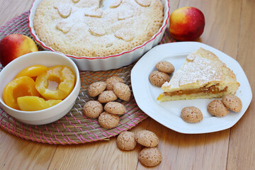 Sweet cake with canned peaches on syrup and italian Amaretti cookies on wooden table