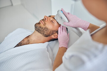 Beautician in sterile gloves treating male skin with laser device