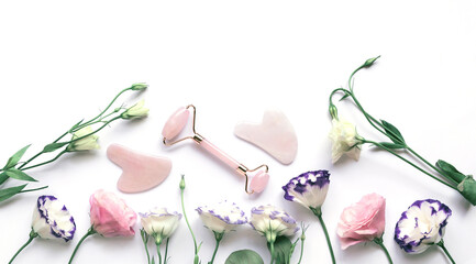 Facial massage kit for home spa. Face roller  and gua sha massager made from rose quartz,   on white background with flowers © Androlia