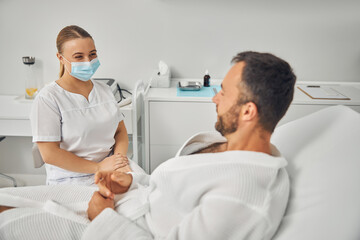 Obraz premium Charming beautician talking with young man in cosmetology cabinet