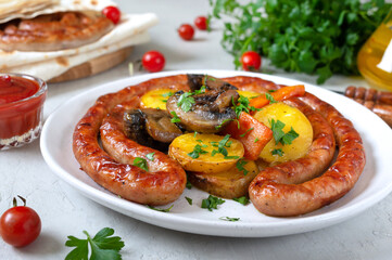 Tasty homemade grilled sausages with baked herb potatoes, mushrooms, cherry tomatoes and ketchup on a wooden background. Oktoberfest snack. Summer picnic dish