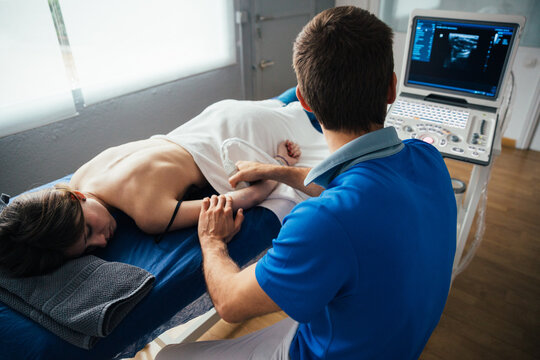 Man therapist doing a muscular ultrasound during a physiotherapy session with a young woman
