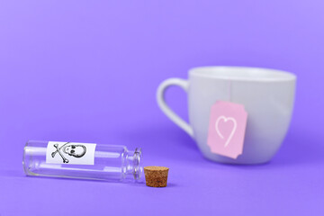 Empty open vial with cork and poison skull label next to white tea cup with heart on label on...