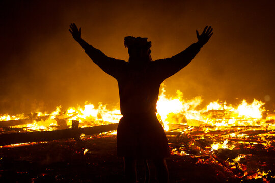 A black silhouette of a man in front of a large fire.