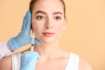 Young woman with acne problem receiving injection in her face against color background
