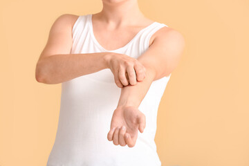 Young woman scratching her skin on color background