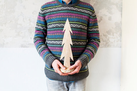 Someone with an old school christmas sweater holding a wooden small christmas tree