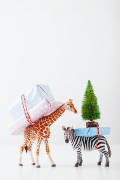 Toy giraffe and zebra carrying Christmas gifts on white.