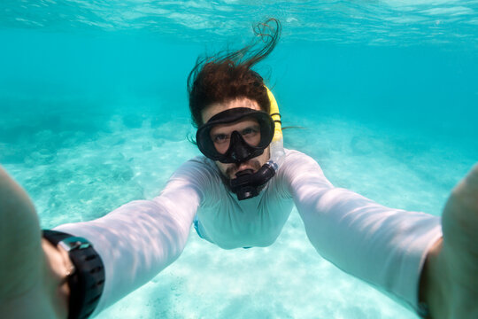 Young man taking selfie while snorkeling in turqoise tropical water of Phi Phi Island in Thailand