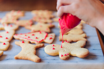 Close up of a child's hand holding a bag of red icing decorating christmas cookes