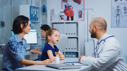 Fototapeta na wymiar Child and doctor talking in clinic while nurse checking pills. Pediatrician specialist in medicine providing health care services consultation diagnostic examination treatment in hospital cabinet