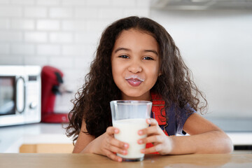 Funny little girl with milk mustache after drinking glass of milk