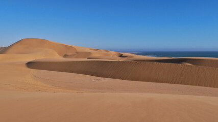 Big beige colored sand dunes with coastline of Atlantic Ocean in background near Swakopmund, Namib desert, Namibia, Africa.